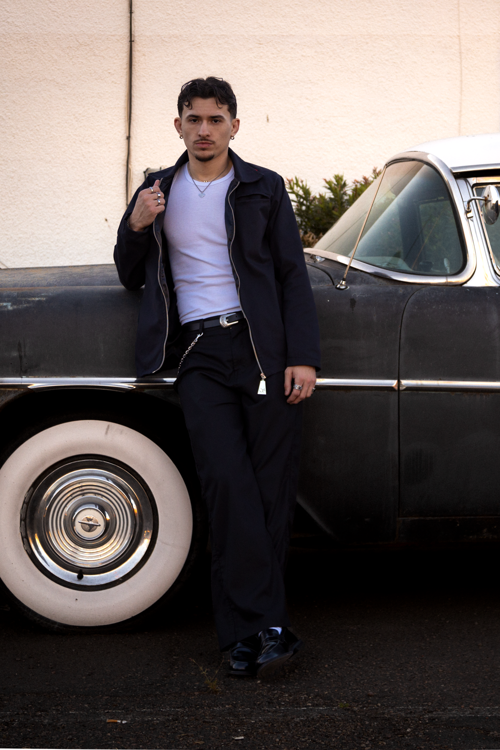 Man standing next to a classic black car with white wall tires.