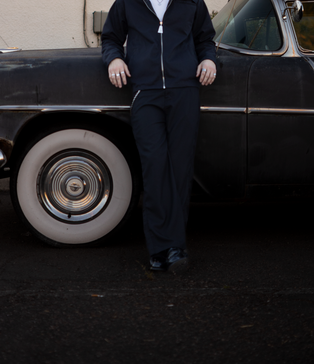 Person standing next to a classic black car in front of a beige building.
