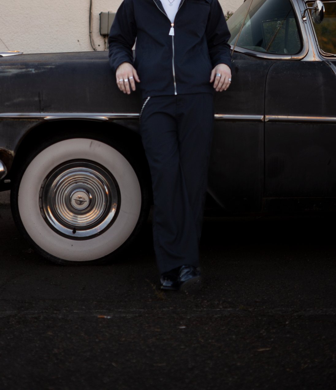 Person standing next to a classic black car in front of a beige building.